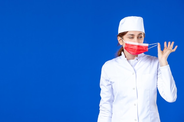 Vooraanzicht van jonge verpleegster in medisch kostuum met rood masker op blauw