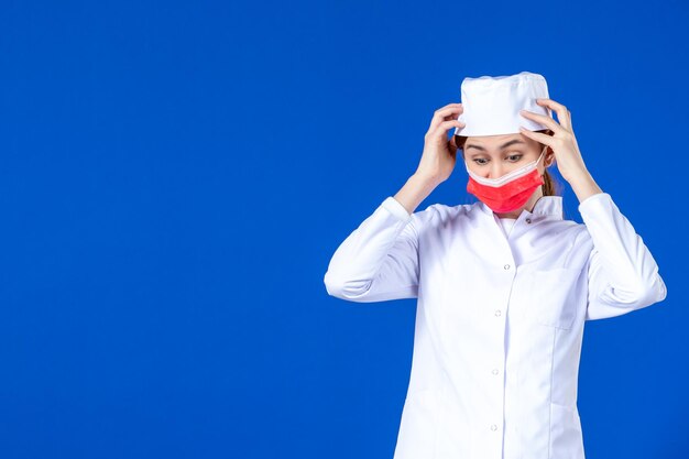 Vooraanzicht van jonge verpleegster in medisch kostuum met rood masker op blauw