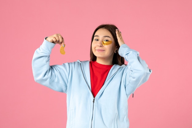 vooraanzicht van jonge vrouw die een gezichtsmasker op roze muur maakt