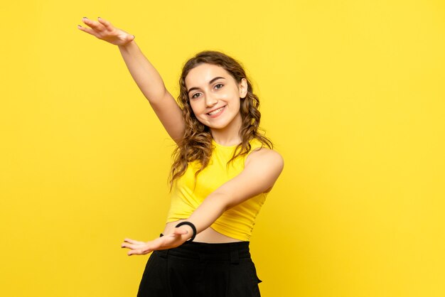 Vooraanzicht van jonge vrouw die en grootte op gele muur glimlacht toont
