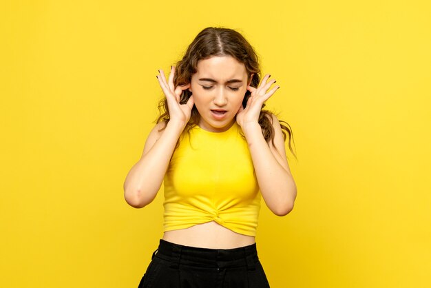 Vooraanzicht van jonge vrouw die haar oren op gele muur sluit