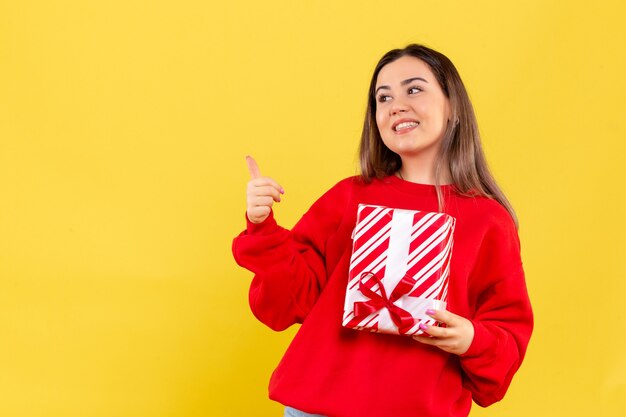 Vooraanzicht van jonge vrouw die kleine gift op gele muur houdt