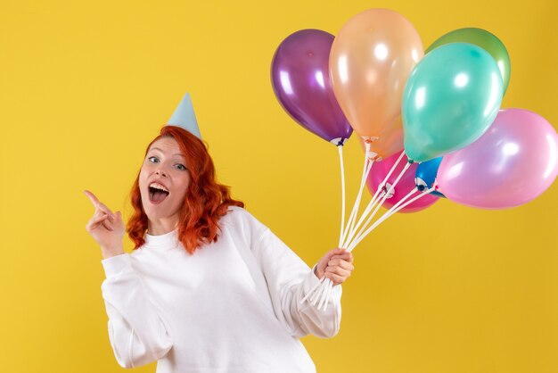 Vooraanzicht van jonge vrouw die leuke kleurrijke ballons op gele muur houdt