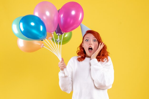 Vooraanzicht van jonge vrouw die leuke kleurrijke ballons op gele muur houdt