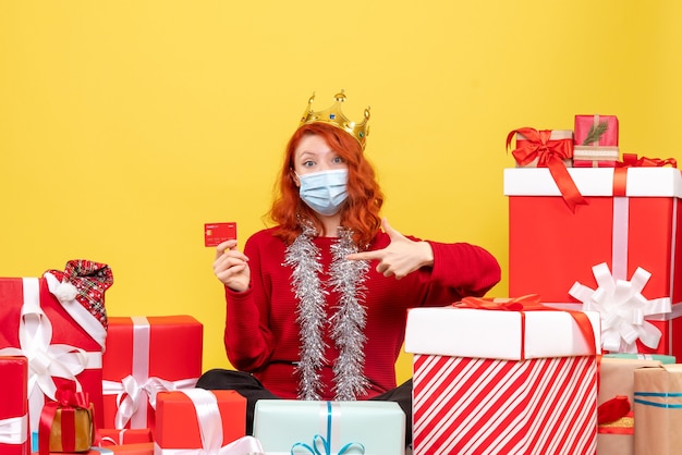 Vooraanzicht van jonge vrouw die rondhangen stelt in masker met bankkaart op gele muur voor