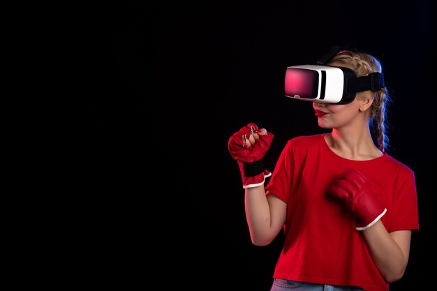 Vooraanzicht van jonge vrouw die vr speelt in mma-handschoenen op de donkere muur