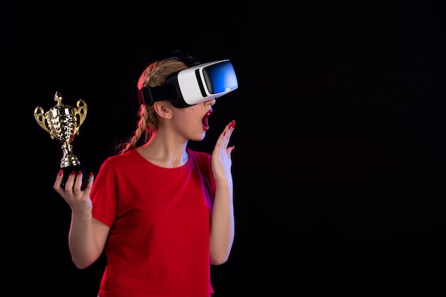 Vooraanzicht van jonge vrouw die vr speelt met winnaarbeker op de donkere muur