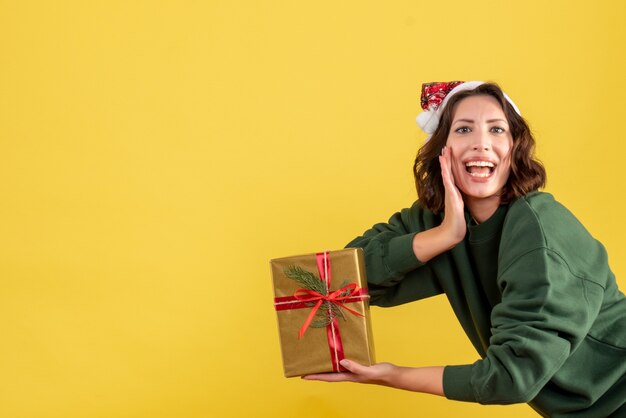 Vooraanzicht van jonge vrouw die weinig Kerstmis op gele muur houdt