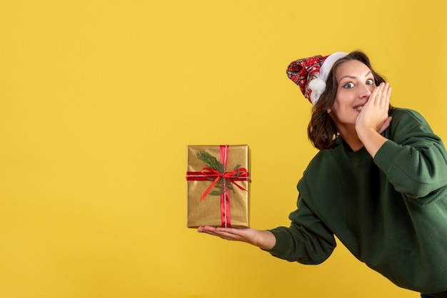 Vooraanzicht van jonge vrouw die weinig Kerstmis op gele muur houdt