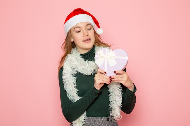 Vooraanzicht van jonge vrouw in rode dop met hartvormig cadeau op roze muur