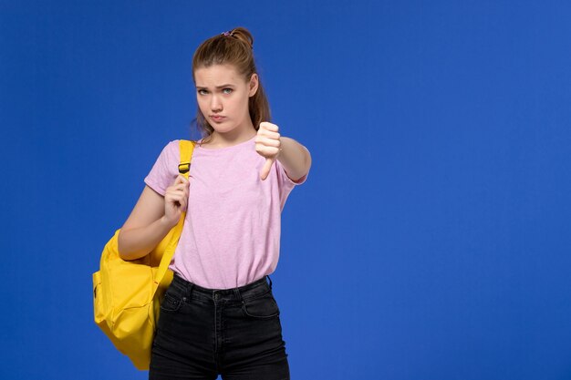 Vooraanzicht van jonge vrouw in roze t-shirt gele rugzak dragen op de lichtblauwe muur