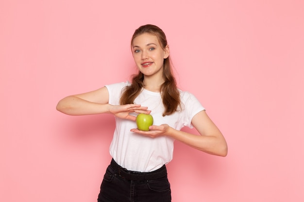 Vooraanzicht van jonge vrouw in wit t-shirt met groene appel poseren op roze muur