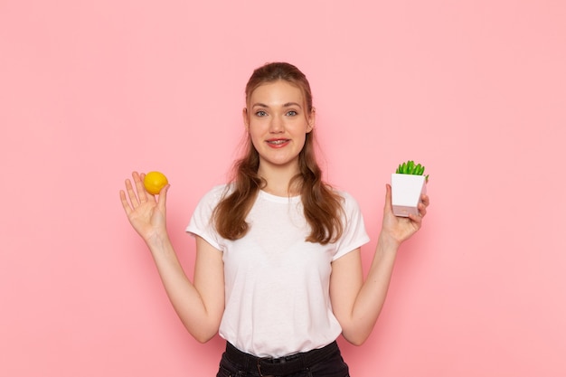 Vooraanzicht van jonge vrouw in wit t-shirt met verse citroen plantje op roze muur