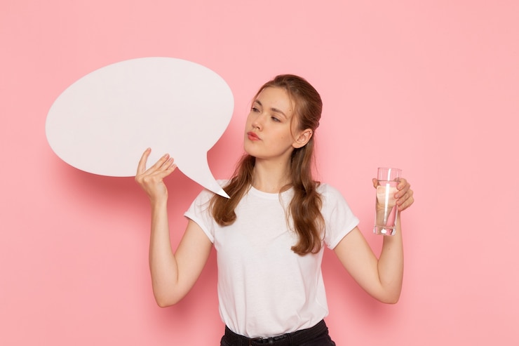 Gratis Foto vooraanzicht van jonge vrouw in wit t-shirt met wit bord en glas water op de roze muur