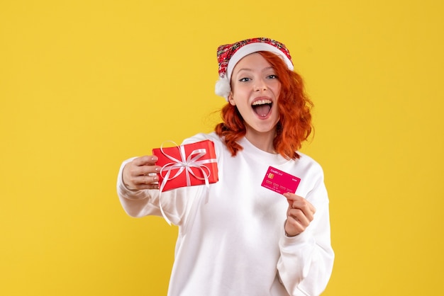 Vooraanzicht van jonge vrouw met aanwezige kerstmis en bankkaart op gele muur