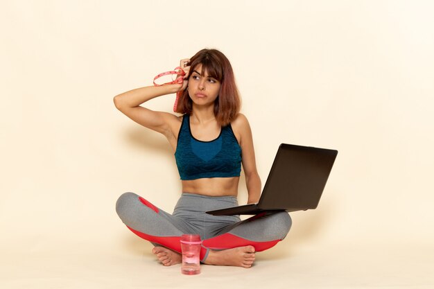 Vooraanzicht van jonge vrouw met fit lichaam in blauw shirt met behulp van laptop op de lichte witte muur