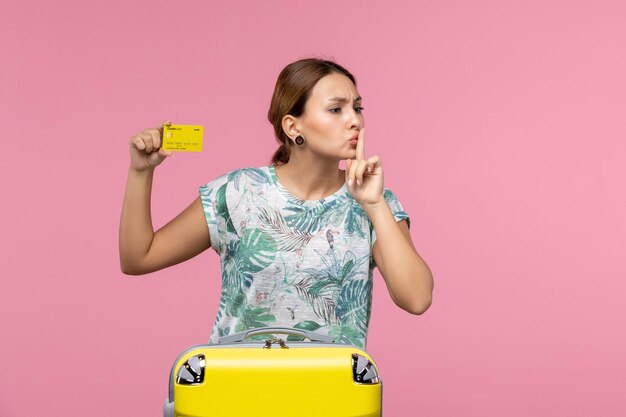 Vooraanzicht van jonge vrouw met gele bankkaart en vakantietas op de roze muur