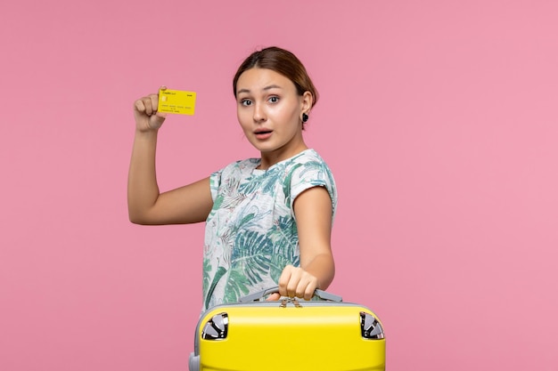 Vooraanzicht van jonge vrouw met gele bankkaart en vakantietas op de roze muur