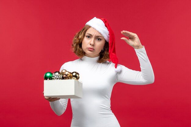 Vooraanzicht van jonge vrouw met kerstspeelgoed op rood