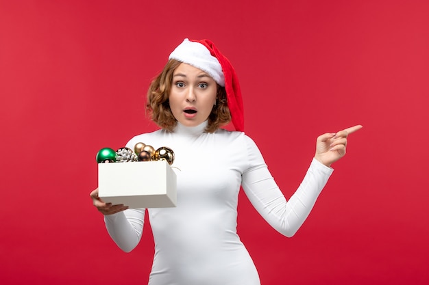 Vooraanzicht van jonge vrouw met kerstspeelgoed op rood