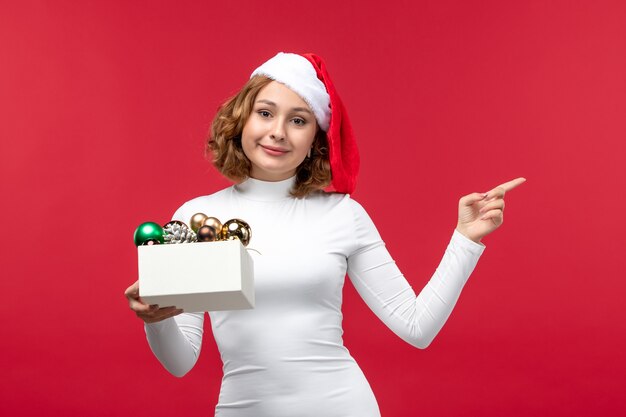 Vooraanzicht van jonge vrouw met kerstspeelgoed op rood