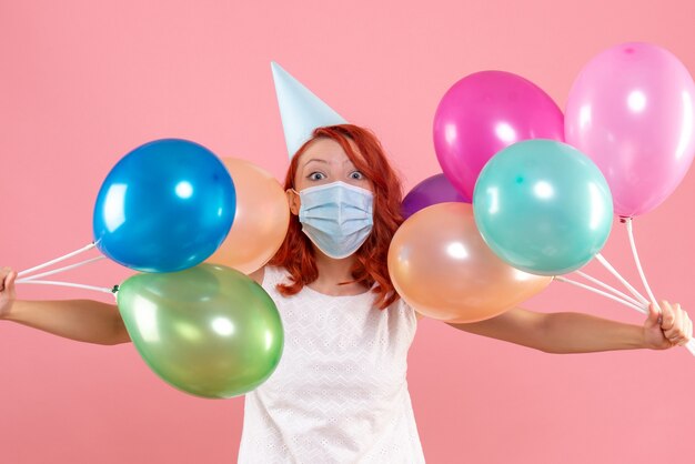 Vooraanzicht van jonge vrouw met kleurrijke ballonnen in steriel masker op de roze muur