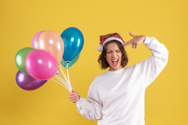 Vooraanzicht van jonge vrouw met kleurrijke ballonnen op de gele muur