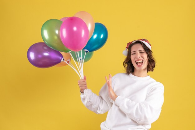 Vooraanzicht van jonge vrouw met kleurrijke ballonnen op de gele muur