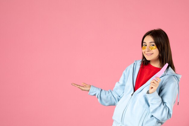 vooraanzicht van jonge vrouw met ooglapjes en nagelvijl op roze muur