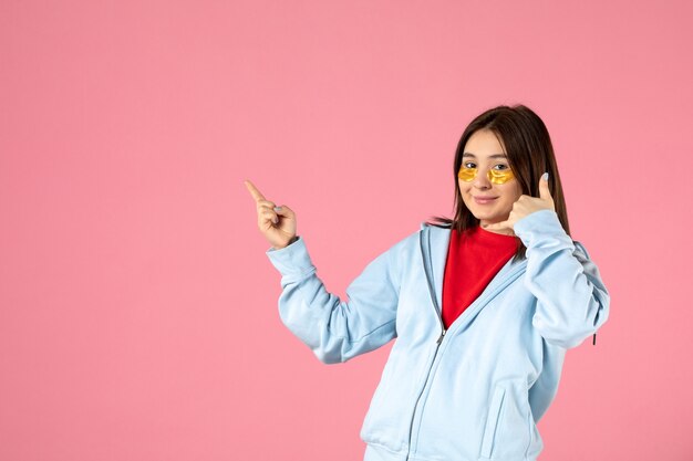 vooraanzicht van jonge vrouw met ooglapjes onder haar ogen op roze muur