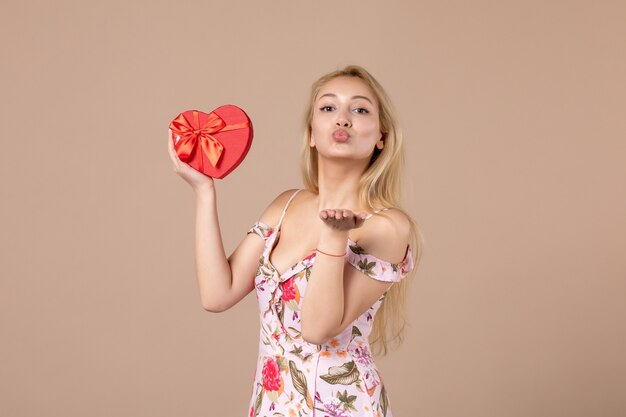 Gratis foto vooraanzicht van jonge vrouw met rood hartvormig cadeau op bruine muur