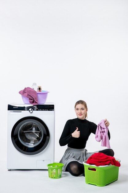 Vooraanzicht van jonge vrouw met wasmachine die vuile kleren op witte muur vouwt