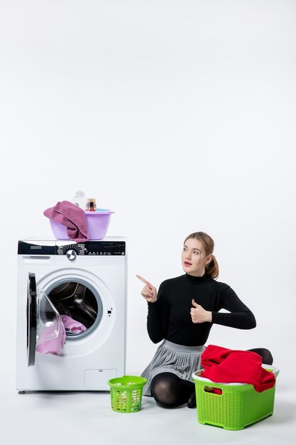 Vooraanzicht van jonge vrouw met wasmachine die vuile kleren op witte muur vouwt