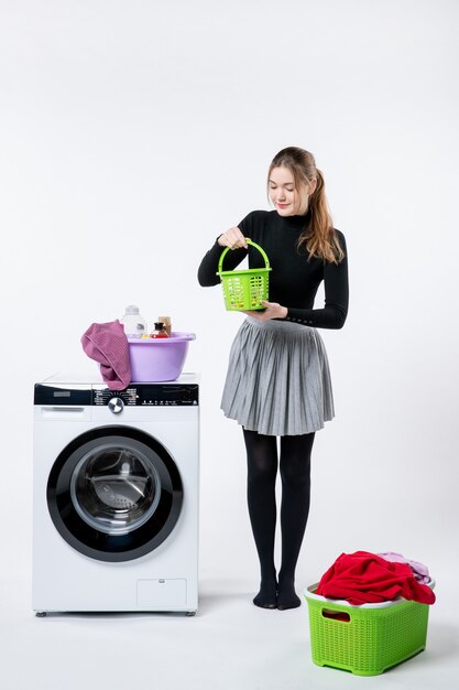 Vooraanzicht van jonge vrouw met wasmachine en vuile kleren op witte muur