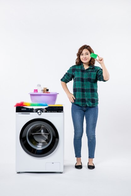 Vooraanzicht van jonge vrouw met wasmachine met groene bankkaart op witte muur