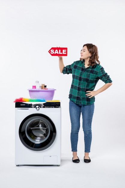 Vooraanzicht van jonge vrouw met wasmachine met verkoopbanner op witte muur