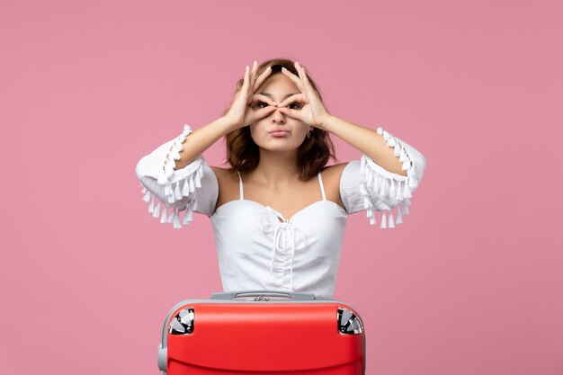 Vooraanzicht van jonge vrouw poseren met rode vakantietas op lichtroze muur