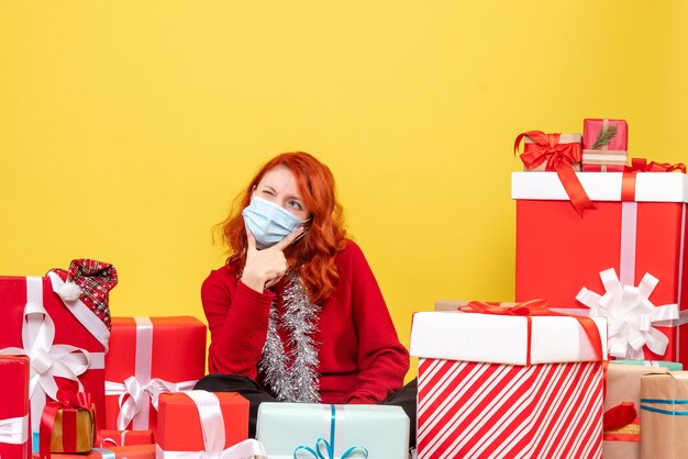 Vooraanzicht van jonge vrouw rond kerstcadeautjes zitten in masker op gele muur