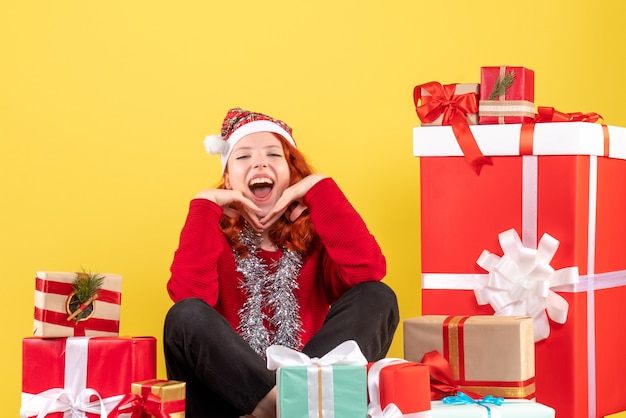 Vooraanzicht van jonge vrouw rond kerstcadeautjes zitten op gele muur