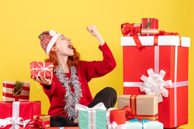 Vooraanzicht van jonge vrouw rond kerstcadeautjes zitten op gele muur