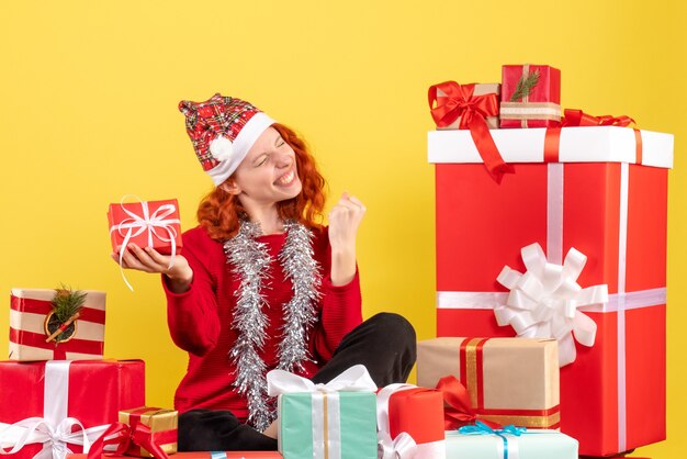 Vooraanzicht van jonge vrouw rond kerstcadeautjes zitten op gele muur