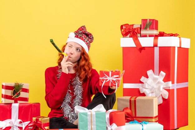 Vooraanzicht van jonge vrouw rond verschillende kerstcadeautjes zitten op gele muur