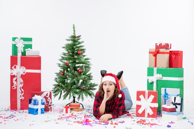 Vooraanzicht van jonge vrouw tot rond kerstcadeautjes en kleine vakantieboom op witte muur