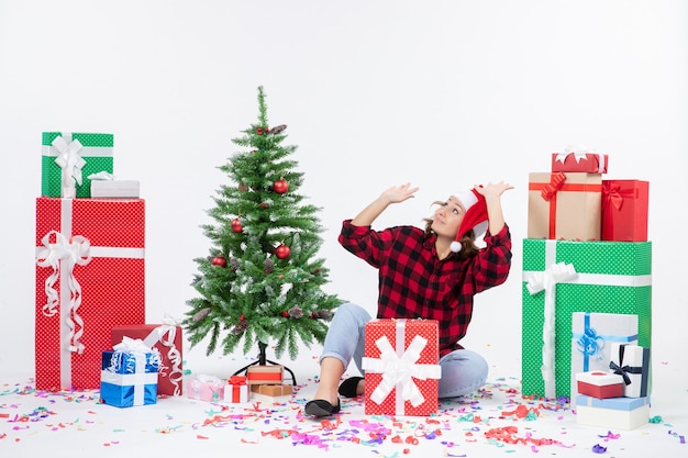 Vooraanzicht van jonge vrouw zitten rond presenteert en kleine vakantieboom op witte muur