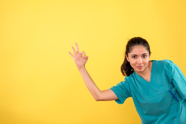 Vooraanzicht van jonge vrouwelijke arts die ok teken op gele muur maakt