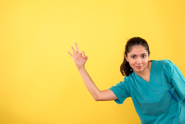 Vooraanzicht van jonge vrouwelijke arts die ok teken op gele muur maakt