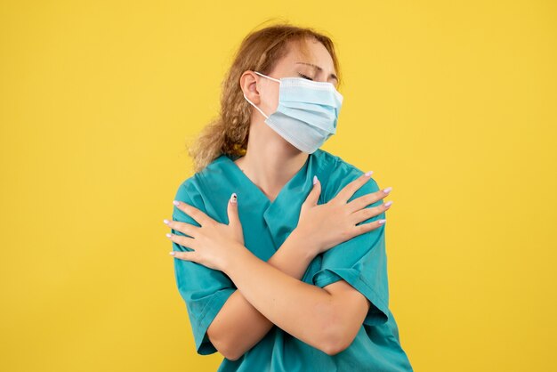 Vooraanzicht van jonge vrouwelijke arts in medisch kostuum en masker op gele muur