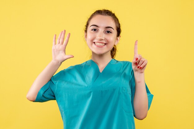 Vooraanzicht van jonge vrouwelijke arts in medisch overhemd op gele muur