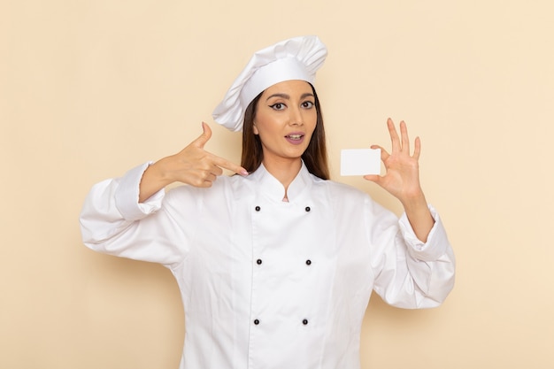 Vooraanzicht van jonge vrouwelijke kok die in wit kokkostuum plastic kaart op lichtwitte muur houdt