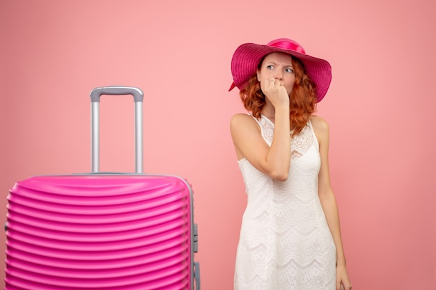 Vooraanzicht van jonge vrouwelijke toerist met roze hoed en tas zenuwachtig op roze muur